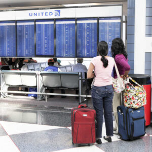 Two Female Travelers Staring At Delta Airlines Check In Desk And Announcement Board At The Airport