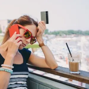 Travel Scam Concept Image Of Woman Holding Her Credit Card While Chatting On The Phone With A View To The Sea