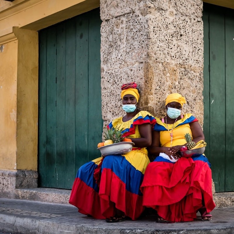 Afrikanska colombianska kvinnor som bär traditionell klädsel och ansiktsmasker i Cartagena, Colombia