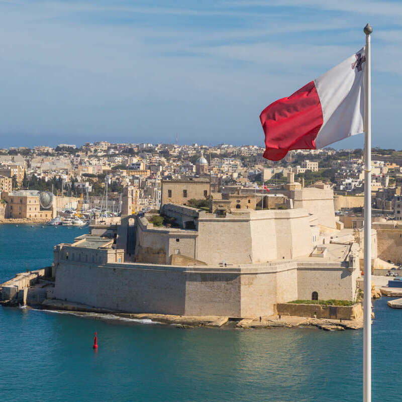 Bendera Malta berkibar dengan latar belakang kota abad pertengahan di Malta, Laut Mediterania, Eropa Selatan