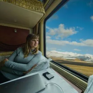 Smiling Female Traveler Taking A Scenic Train Journey With Snowy Mountains For A View