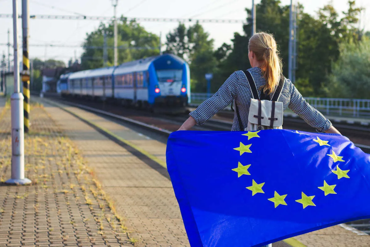 Female traveler holding up a European Union flag as a train approaches the station, unspecified location
