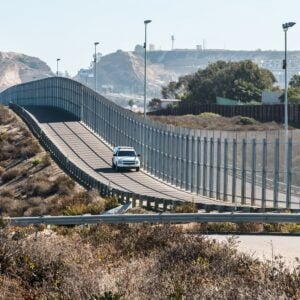 San Diego, California and Tijuana, Mexico international border wall with border patrol vehicle.