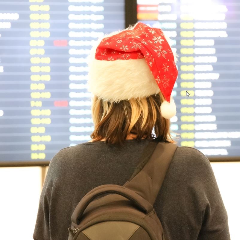 Traveler looking at flight board with santa holiday hat on