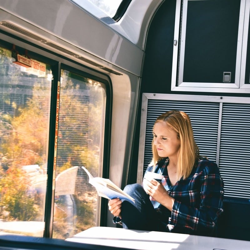 Female traveler reading a book drinking coffee or tea while traveling by train, travel concept