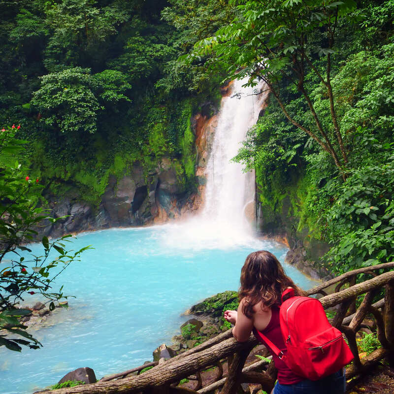 Ung kvinnlig turist med en ryggsäck som tittar på ett vattenfall i en naturlig miljö, Costa Rica, Centralamerika