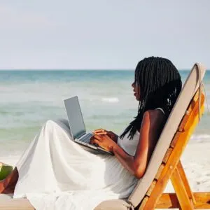 Young woman enjoying sitting on chaise-lounge, working on laptop, ocean in the background