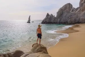 Young Male Tourist Standing On A Rock Formation At The Beach, Baja California Sur, Pacific Coast Of Mexico