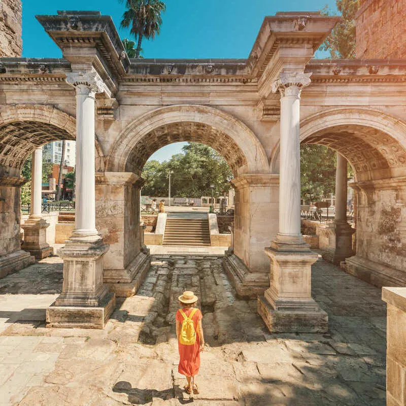 Young Female Tourist Crossing Hadrian's Gate In Kaleici, Old Town Antalya, Turkey