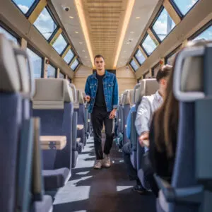 a man walks down the aisle of the GoldenPass express train with windows for scenery all around