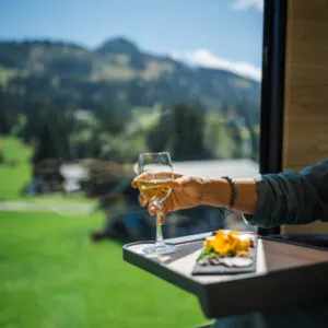 A person holds a glass of white wine wile sitting on the GoldenPass Train in Switzerland with scenic views out the window
