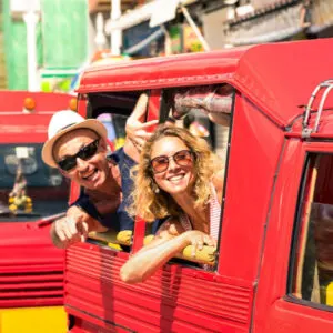 two tourists hang their heads out of a red tuk tuk in Phuket Thailand