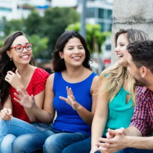 A group of young people sit on a bench and practice speaking Spanish together