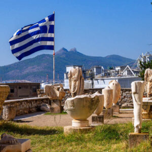 Greek Flag Flying On A Pole In The Exterior Area Of The Archaeological Museum Of Elefsinas, Surrounded By Hellenic Monuments And Sculptures, West Attica Region Of Greece, Southeastern Europe