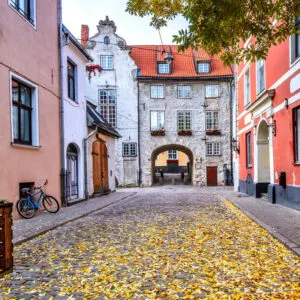 Medieval Street Lined With Colorful Buildings Leading To An Old Stone Gate In Old Town Riga, Latvia, Eastern Europe
