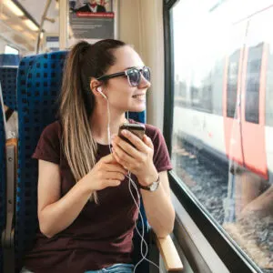 A Young Woman Listening To Music On Her Headphones As She Admires The View Traveling On A Train, Unspecified Location