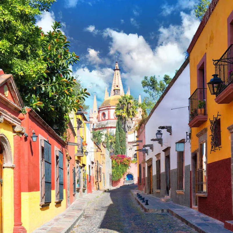 Cobblestone Alleyway Lined With Colorful Colonial Era Houses Leading To A Pink Church Spire In San Miguel de Allende, Mexico