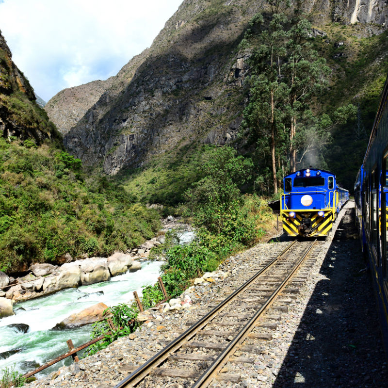 Train traveling through a mountain valley alongside a river