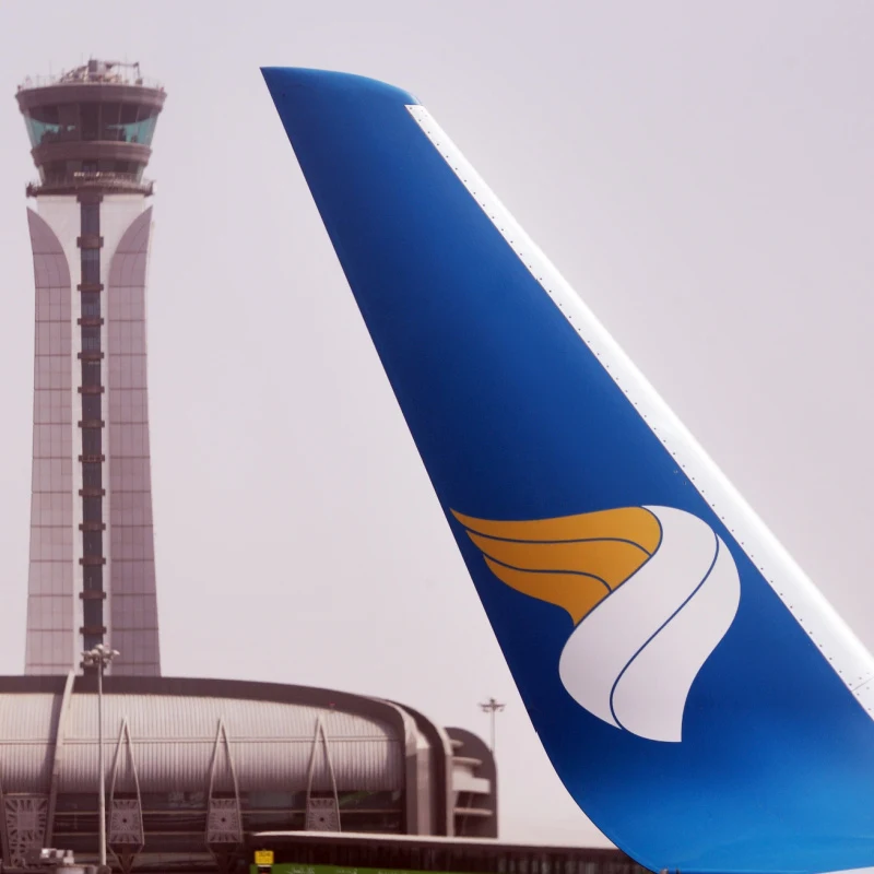 Blue, white, and gold airline wing in front of a tower.