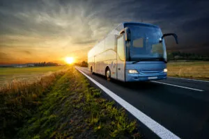 Bus traveling on the asphalt road in rural landscape at sunset.