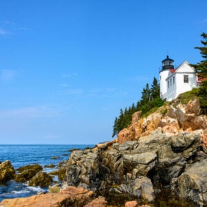 a white lighhouse sits on the edge of a rocky shore in Maine