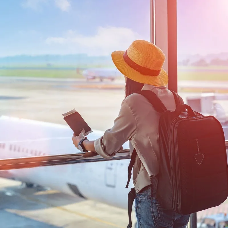 Female traveler observes aircraft approaching the tarmac while holding her passport at an international airport