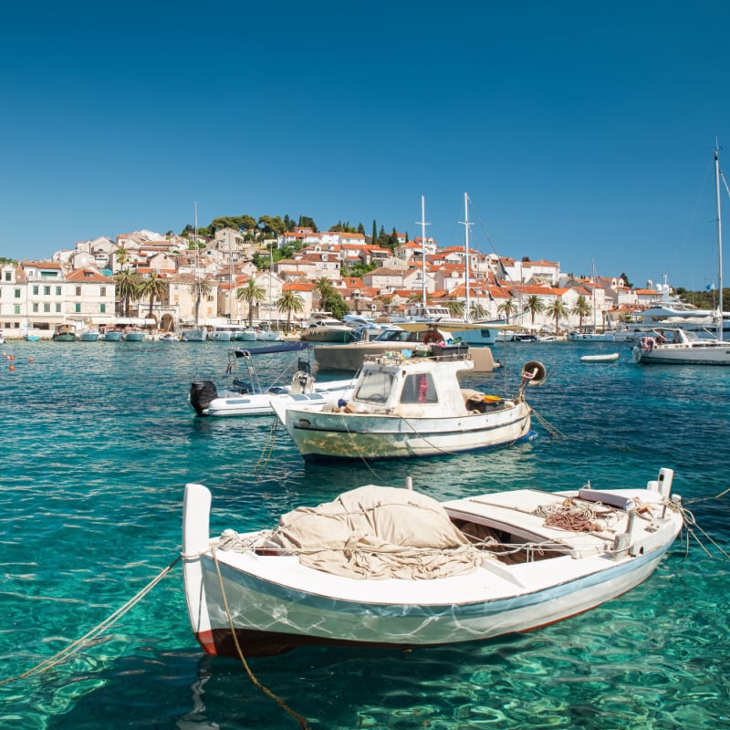 Hamn med båtar i turkosa vatten på ön Hvar, Kroatien med gamla stan i bakgrunden.  Turistort.  Sommarsemestermål. 