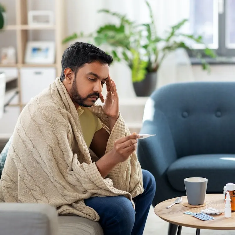 sitting man measuring his body temperature with thermometer