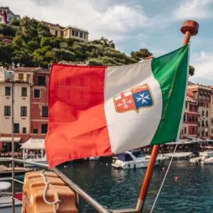 Italian Flag Flying With The Port Of Portofino Blurred In The Backgrond, Ligurian Sea, Italy