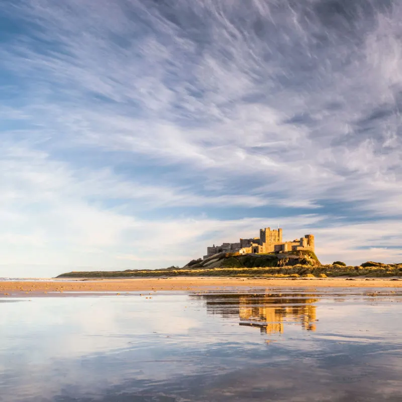 A view of Bamburgh castle reflected in the water of the beach below.