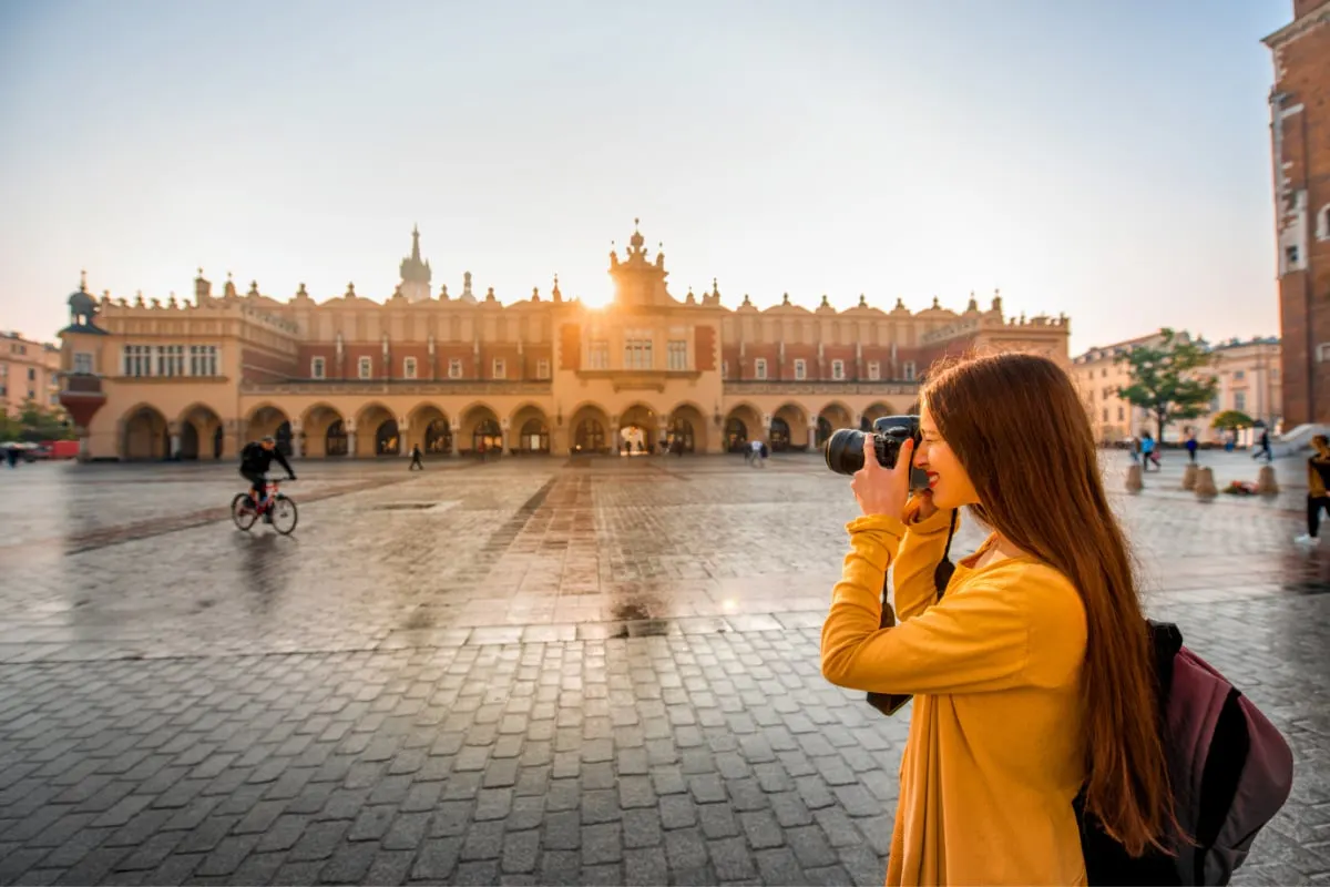 Young female tourist with camera and backpack photographing Cloth Hall in the old city center of Krakow (1)