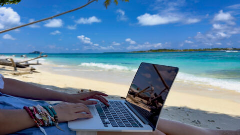 Nomad digital with laptop and running remotely with bright scenic view near poolside on the beach in summer time