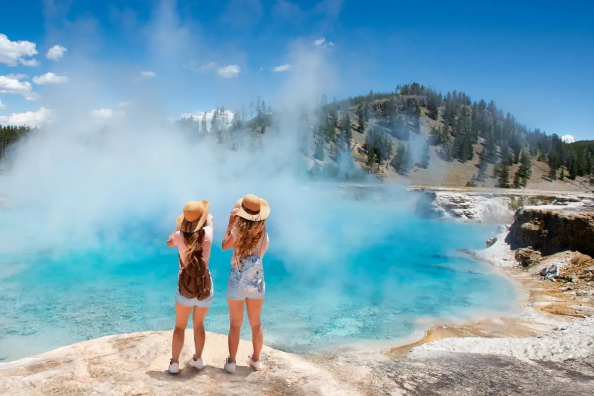 Girls relaxing and enjoying beautiful view of gazer on vacation hiking trip. Friends on hiking trip. Excelsior Geyser from the Midway Basin in Yellowstone National Park. Wyoming, USA