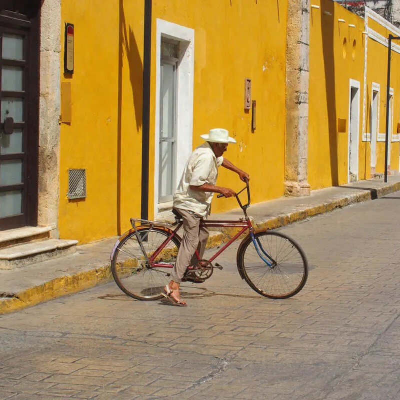 Mexican Man Riding His Bike Through The Yellow Streets Of Colonial Izamal, In The Yucatan Peninsula Of Mexico, Latin America