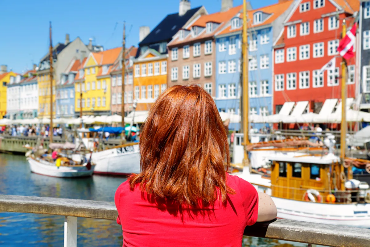 Woman enjoying the scenic view of Nyhavn pier. Colorful building facades with boats and yachts in the Old Town of Copenhagen, Denmark