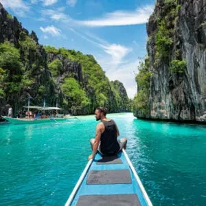 A Male Tourist Sitting On The Tip Of A Long Tail Boat In El Nido, Palawan, Philippines, Southeast Asia