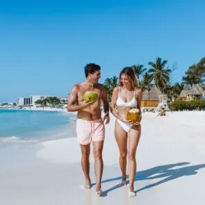 A Young Couple Looking Happy As It Walks Down A Beach Drinking Coconut Water In Tulum, A Mayan Beach Town Bounded By The Caribbean Sea, Mexico, Latin American