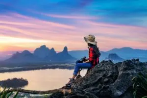 Young Female Tourist Perched On A Rock In Phu sub lek Overlooking A Tropical Landscape, Thailand, Southeast Asia