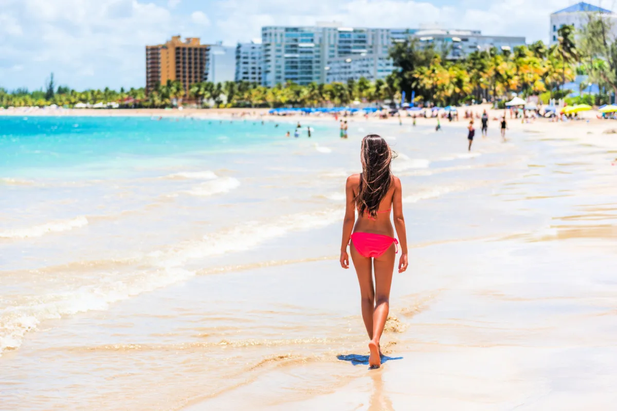 People on Isla Verde resort beach in Puerto Rico. Unrecognizable woman walking down the beach on summer holiday in bikini on famous Hispanic travel destination