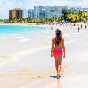 People on Isla Verde resort beach in Puerto Rico. Unrecognizable woman walking down the beach on summer holiday in bikini on famous Hispanic travel destination