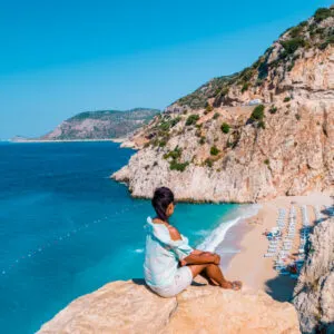 young woman sitting on a rock looking out over the cliff of Kaputas Beach Turkey Mediterranean Sea by Kas, View of the Kaputas Beach, Turkey