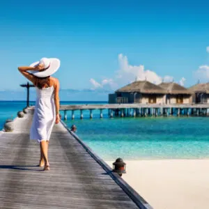 woman walks along boardwalk in stunning maldives resort with beach huts