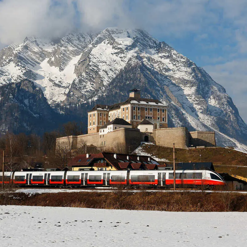 Austrian OBB Train Passing By A Medieval Castle In Austria, With A Snowy Mountain For Background, Central Europe