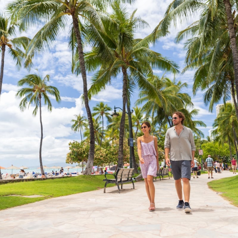 Honolulu city travel tourists couple walking on Waikiki beach boardwalk