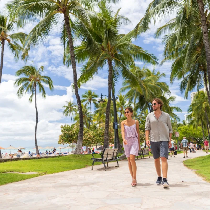 Travelers Can Now Reach Hawaii's Most Popular Airport By Train For The First Time Ever Honolulu city travel tourists couple walking on Waikiki beach boardwalk