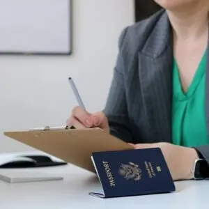 An Official Writing Something On A Sheet Of Paper As An American Passport Rests On The Tabletop.jpg
