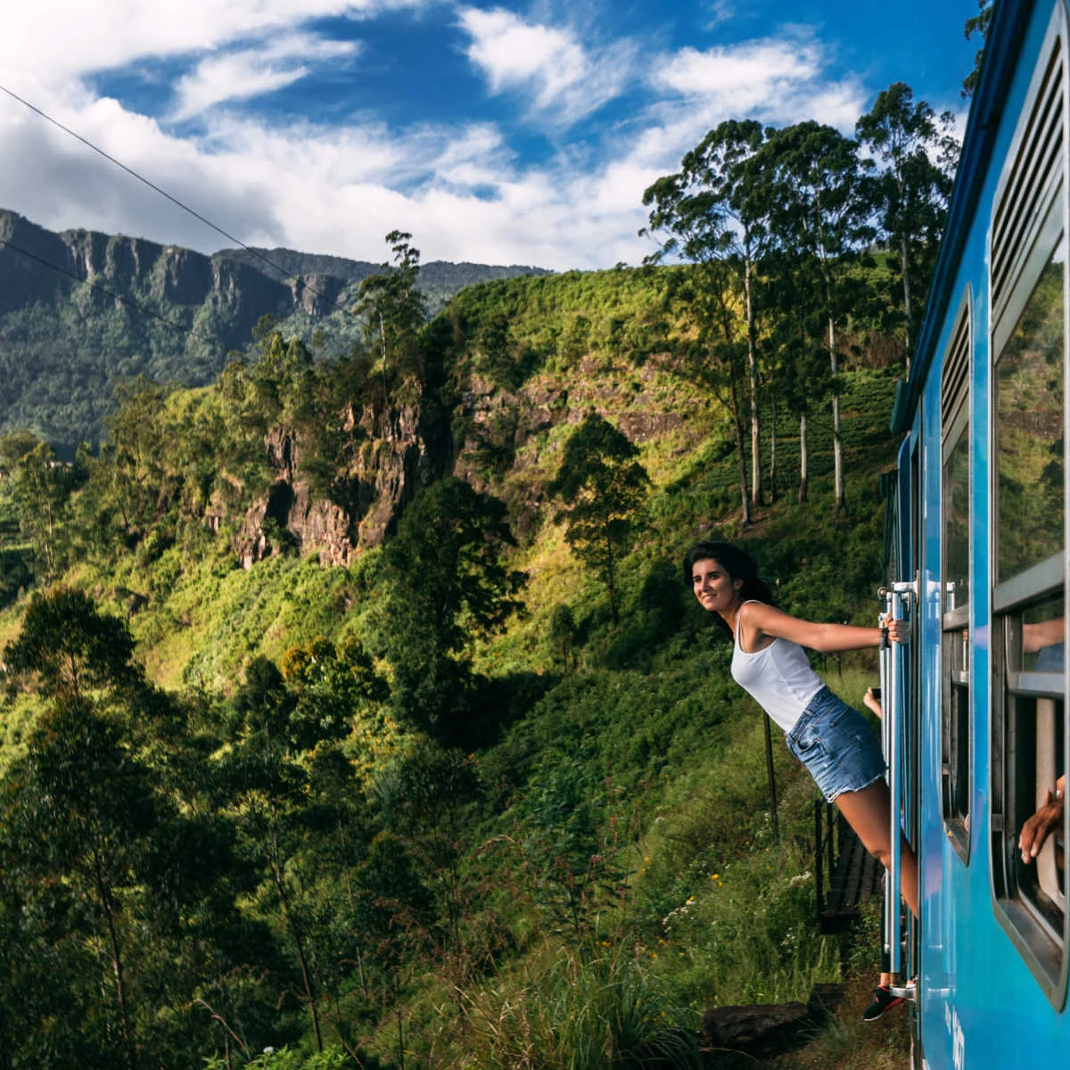 Woman hanging out of train passing through astounding Sri Lanka scenery