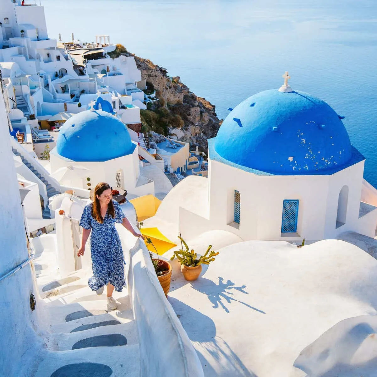 Young Woman Climbing Up The Steps Of Oia, Santorini, Greece