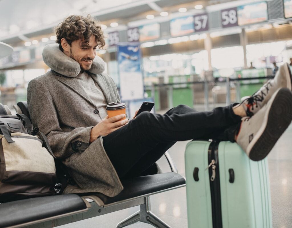 Man at airport waiting for flight checking travel advisories on phone