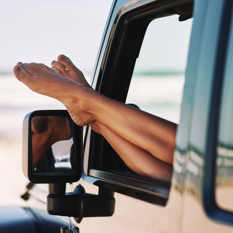 A Woman Relaxing In A Car Barefoot, Near A Beach Location